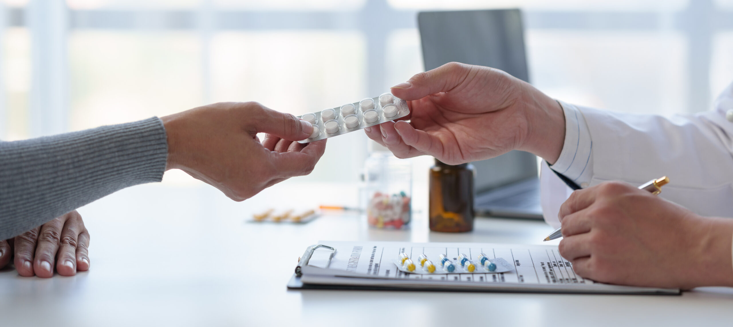 Pharmacist handing prescription drugs to woman across the table, and filling out paperwork on a clipboard. These are examples of prescription drugs that could be more affordable with Medicare's new negotiated prices.