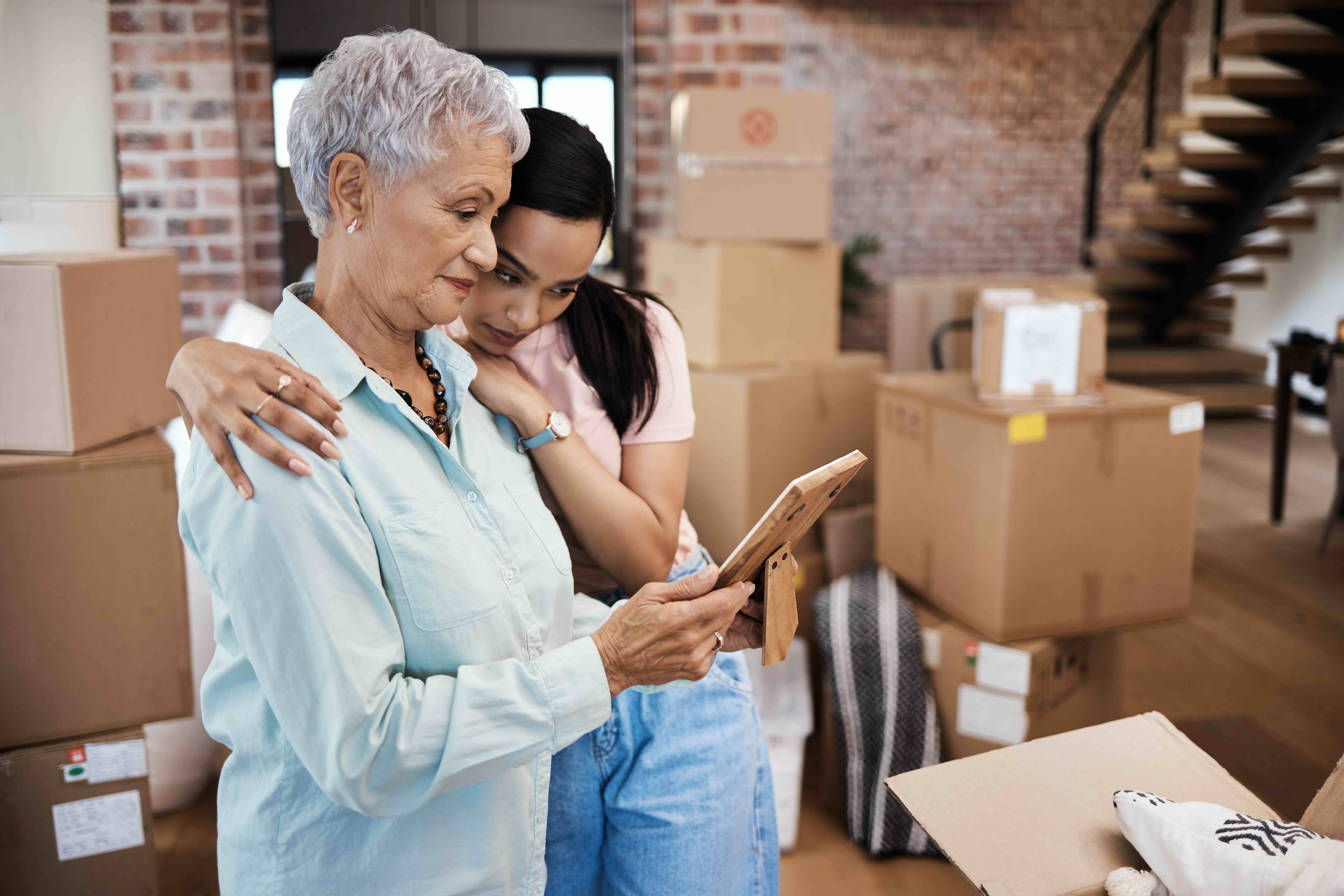 Shot of a senior woman looking at a photograph with her daughter while packing boxes on moving day. Moving is one of the qualifying life events that may impact your healthcare coverage.