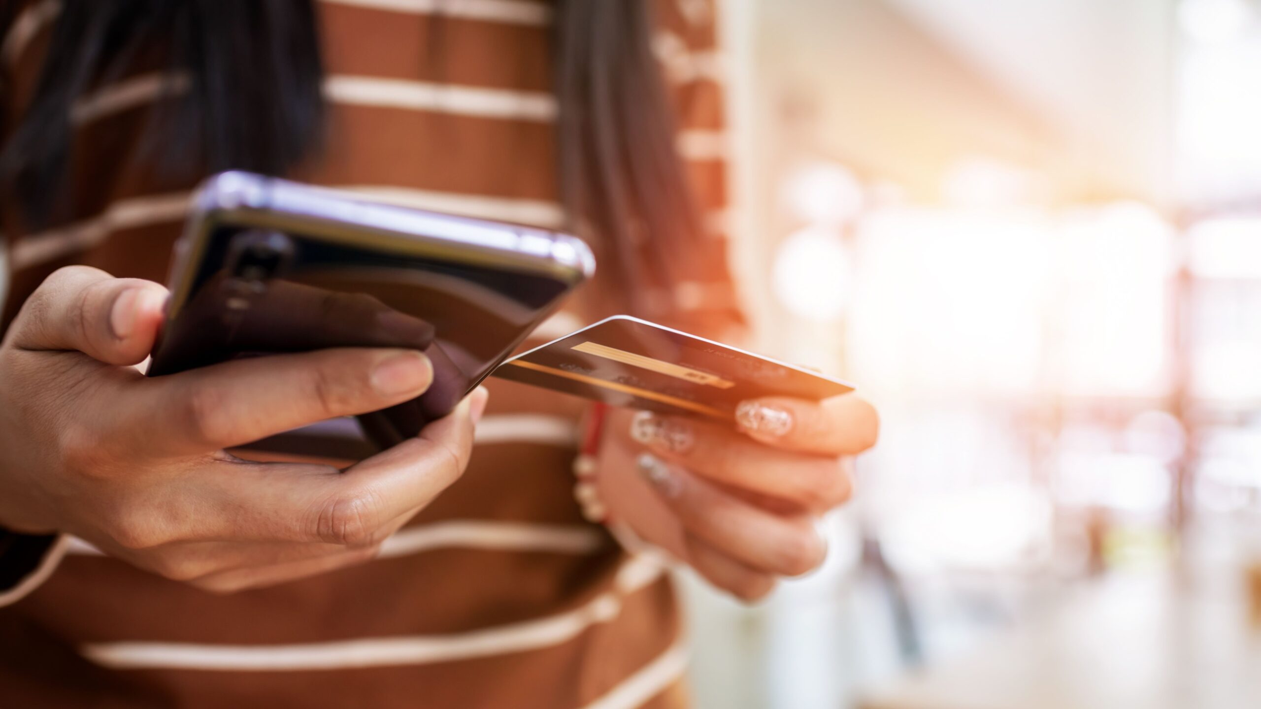 Close up young woman hands holding credit card and using mobile smart phone. Learn online shopping safety tips to protect your credit card information and avoid scams.
