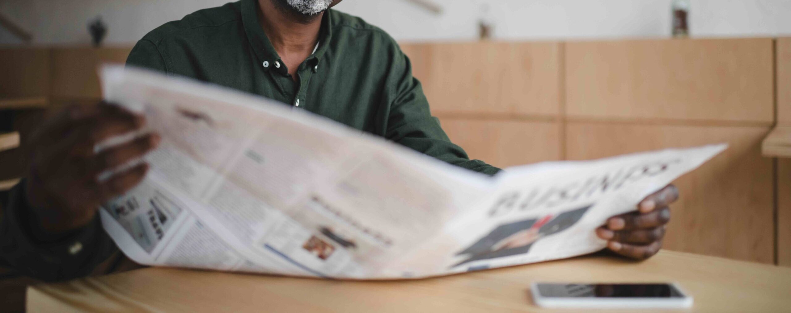Older black man reads a newspaper at a table, a concept for reading news about the Big Beautiful Bill - a tax bill signed into law