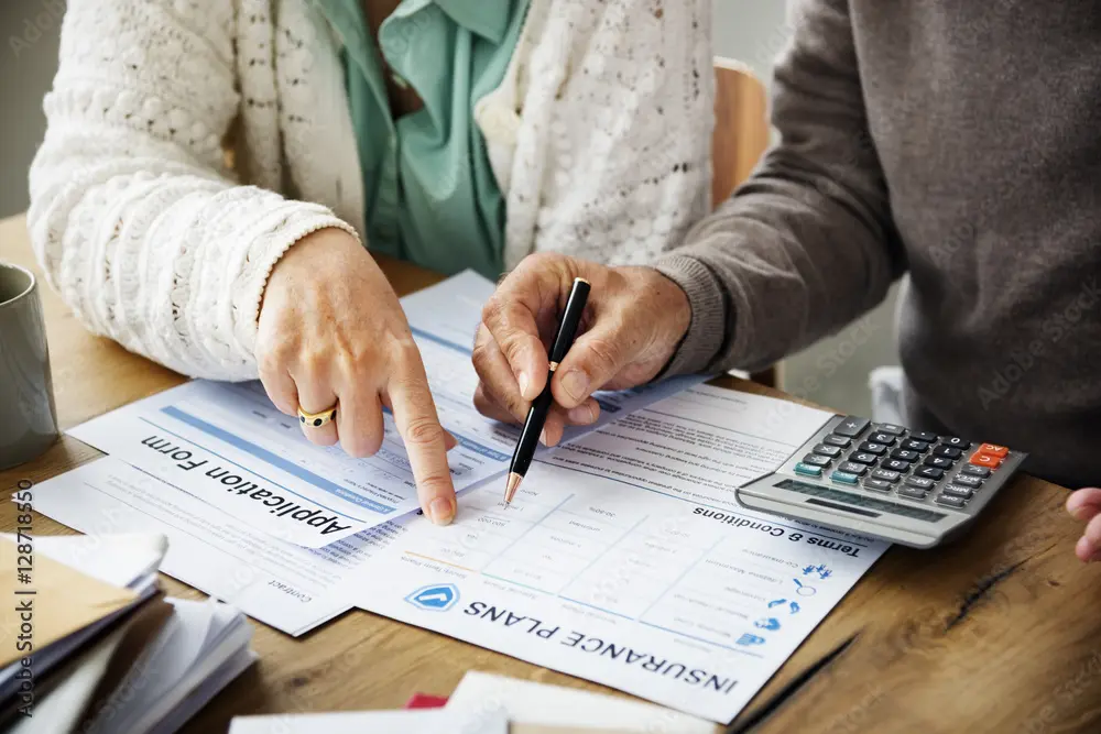 A couple compare insurance plan benefits and application forms at a table with a calculator. Concept for Medicare Advantage new member checklist.
