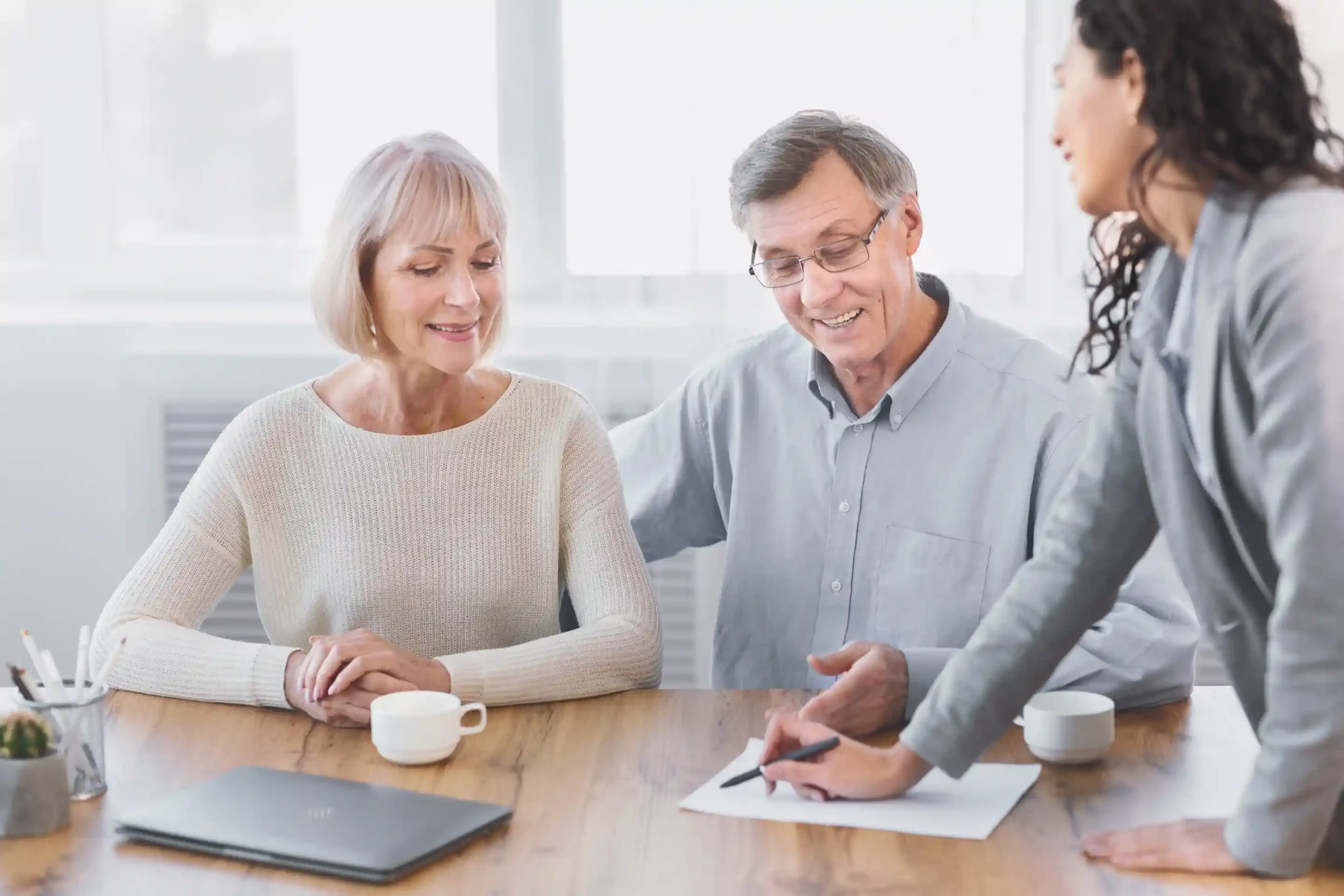 Senior couple speaks with an advisor in an office. The advisor writes on a document with a pen.