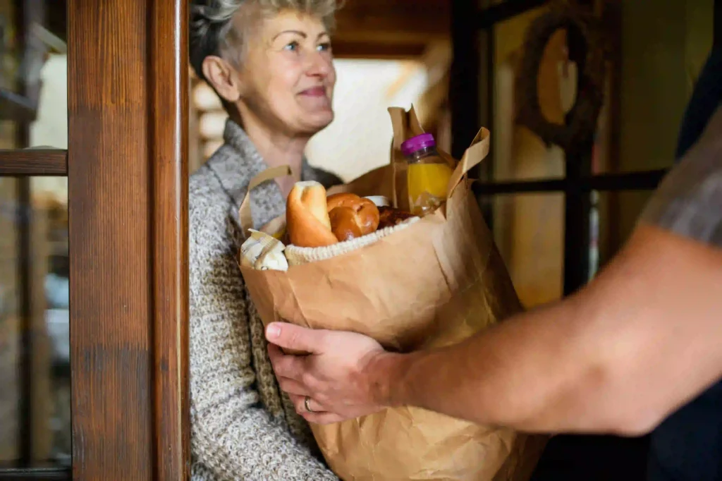 An older woman receives a bag of groceries from a delivery person at her front door