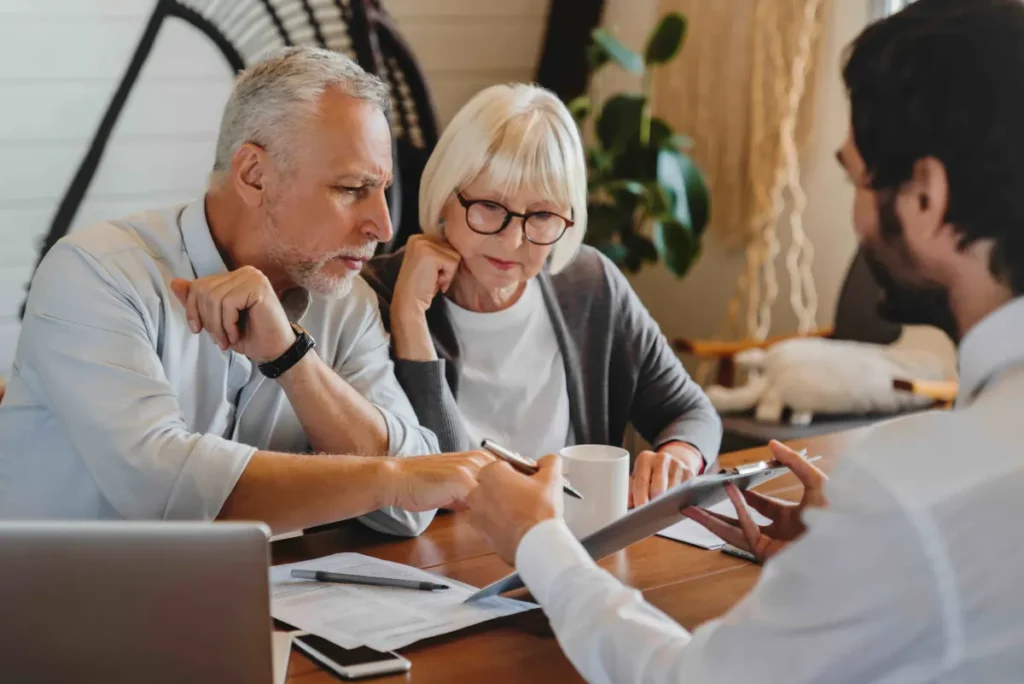 An older couple looks closely at a document being held by a Medicare advisor across a desk.